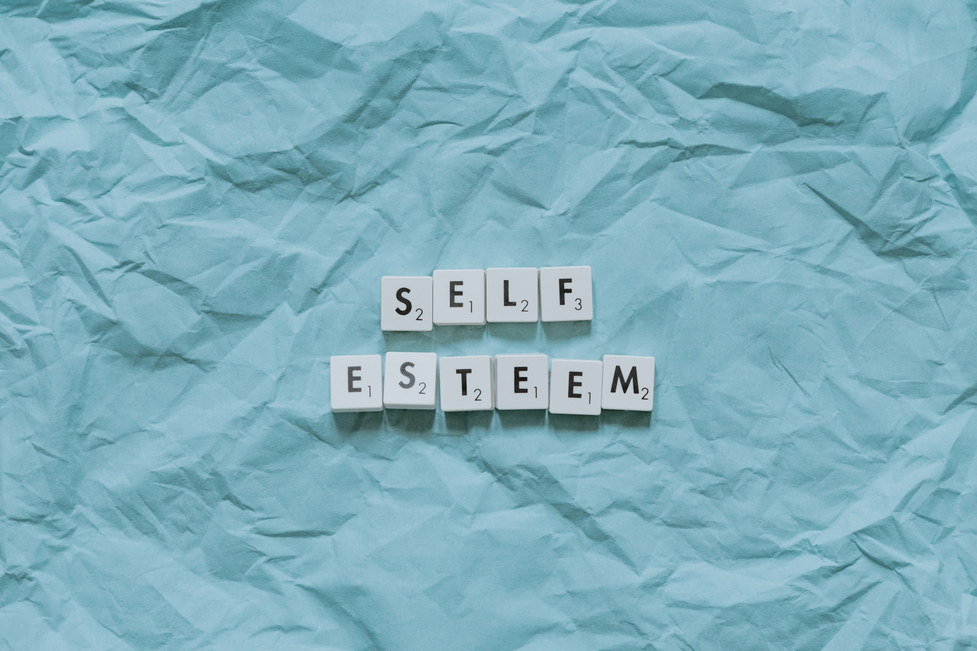 Piese de Scrabble cu cuvintele self esteem pe fundal albastru — ilustrație pentru articolul despre stima de sine